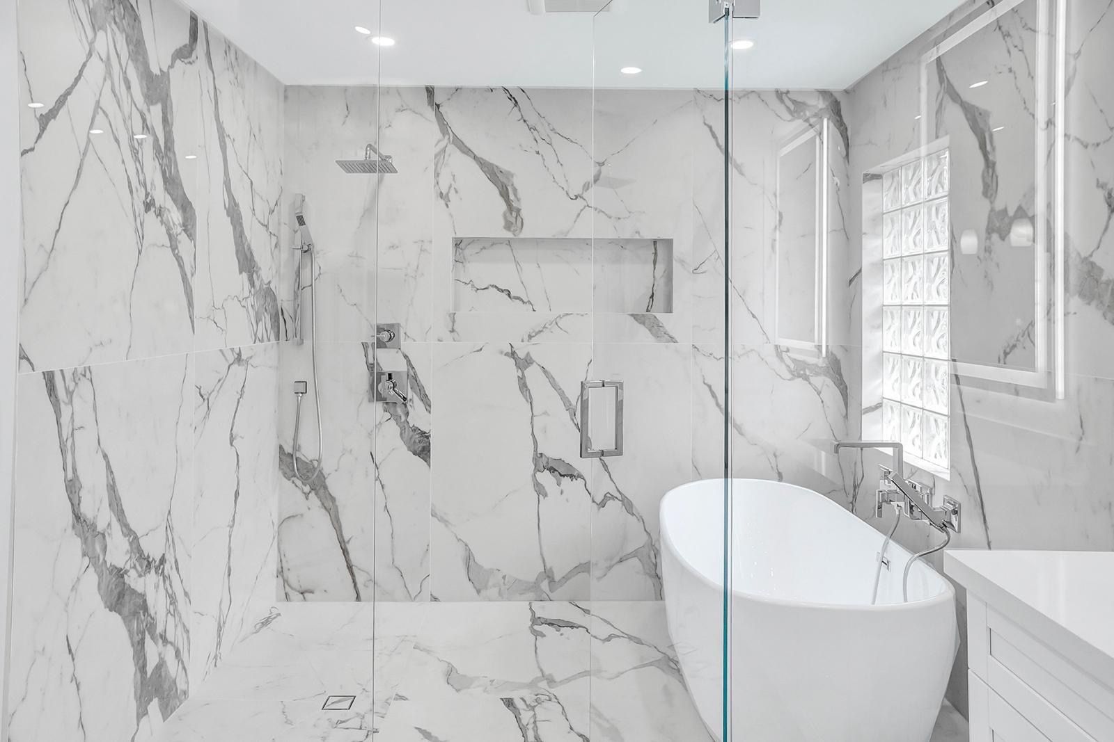 A bathroom with marble walls , a walk in shower , a bathtub and a sink.