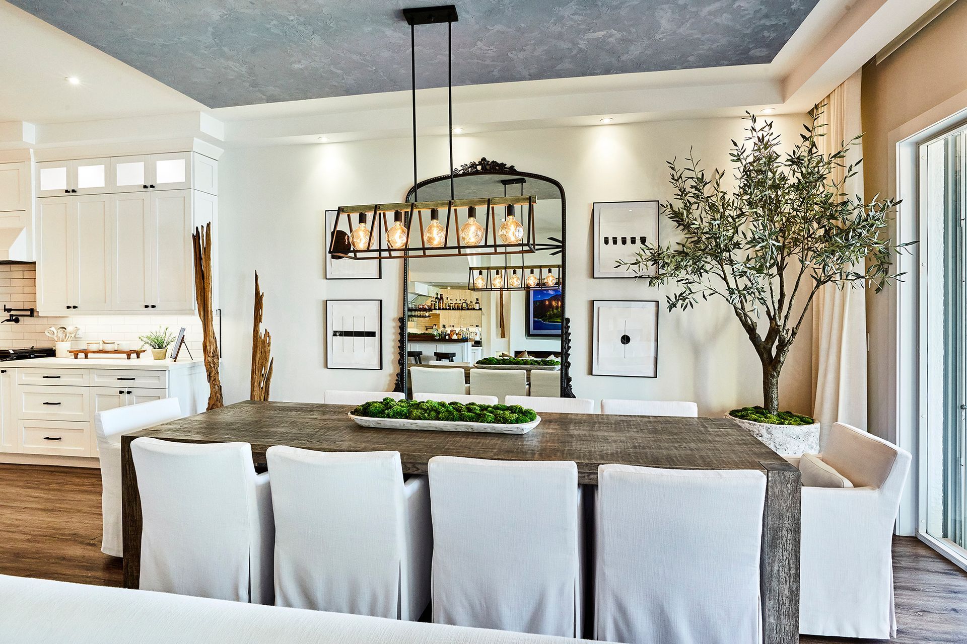 A dining room with a table and chairs and a mirror hanging from the ceiling.