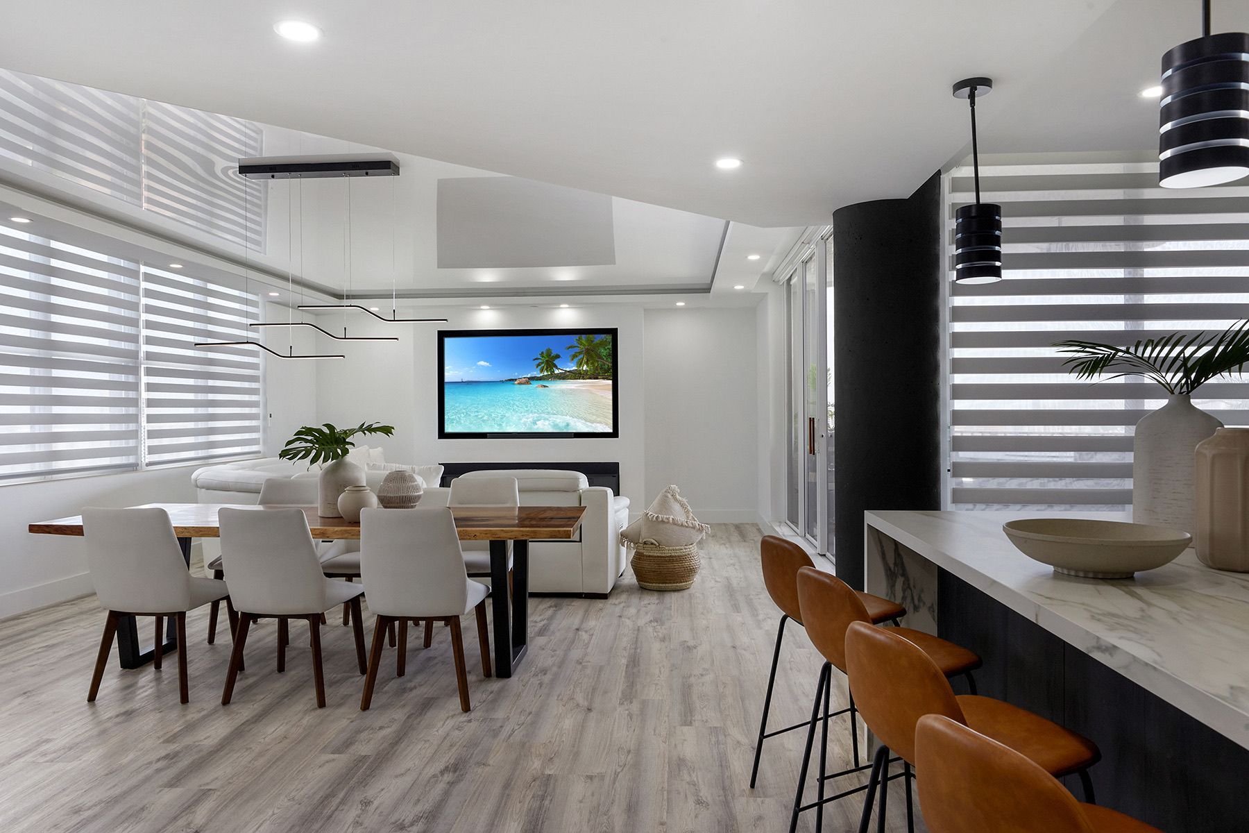 A living room with a dining table and chairs and a flat screen tv on the wall.