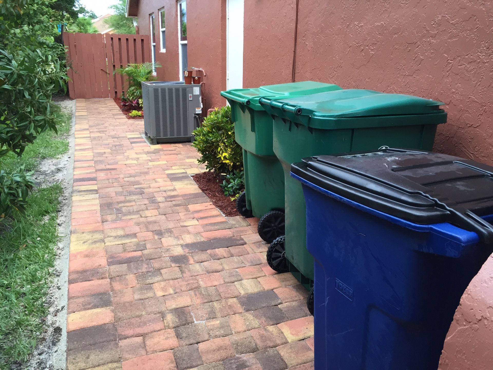 A row of trash cans on a sidewalk next to a house