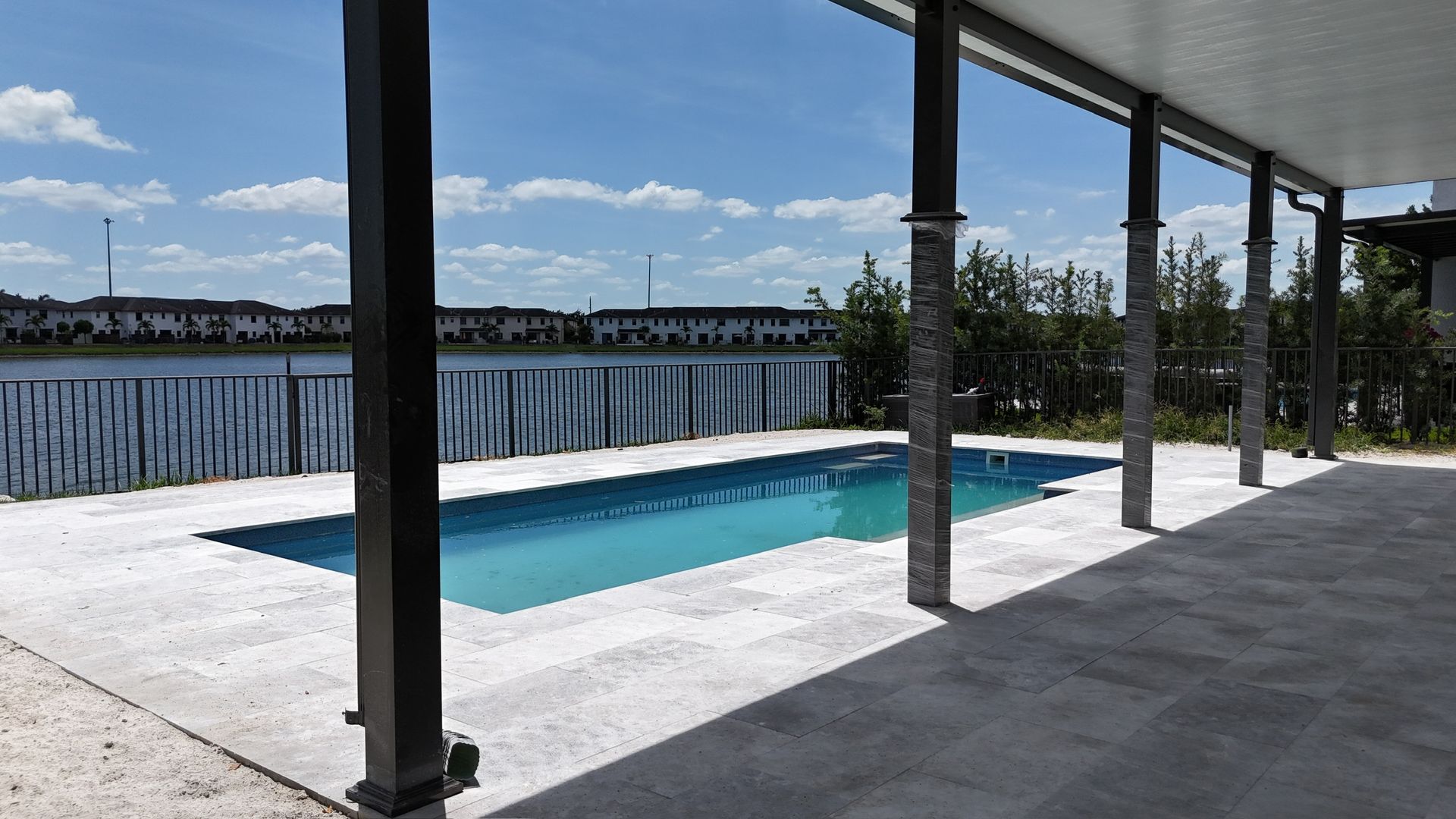 A large swimming pool is surrounded by a covered area with a view of the water.