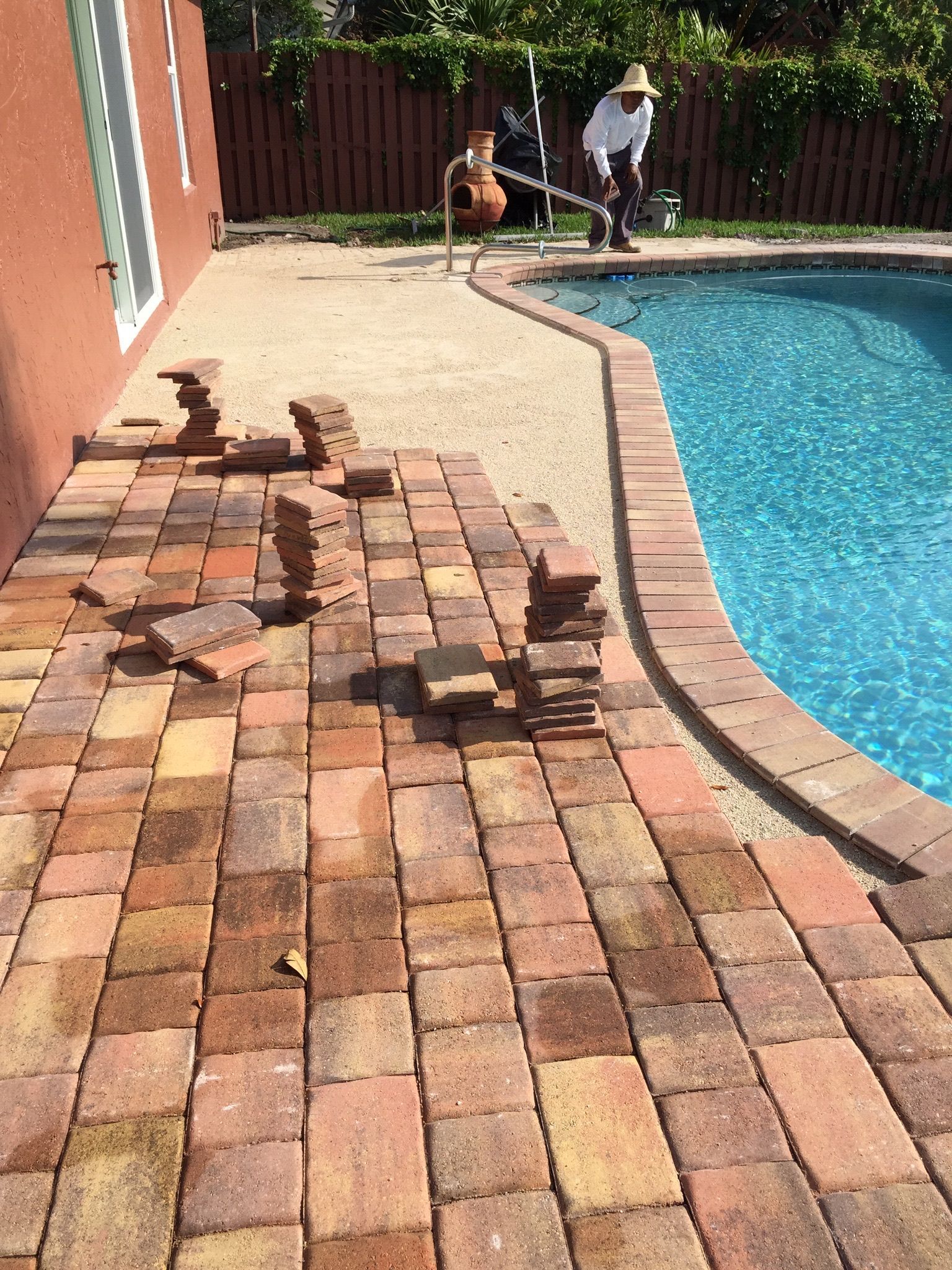 A man is laying bricks next to a swimming pool.