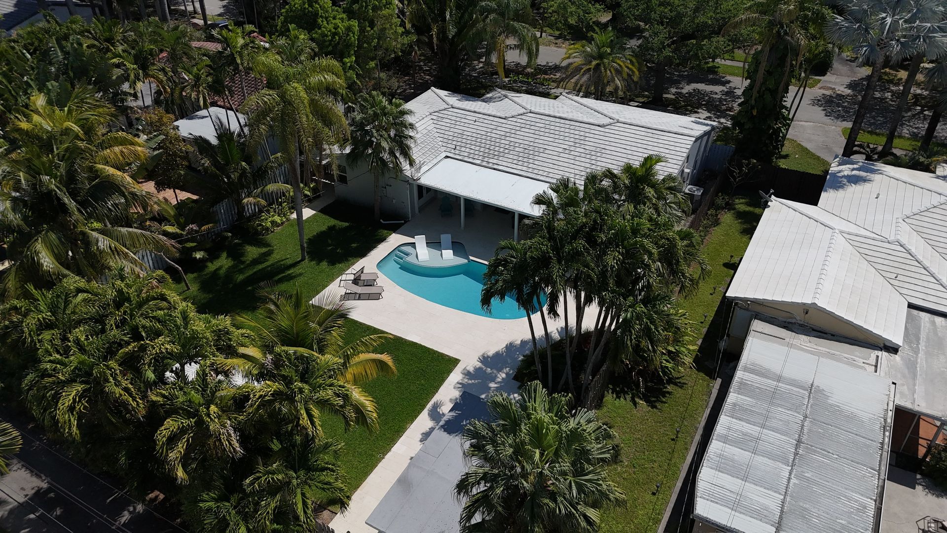 An aerial view of a house with a pool in the backyard surrounded by palm trees.