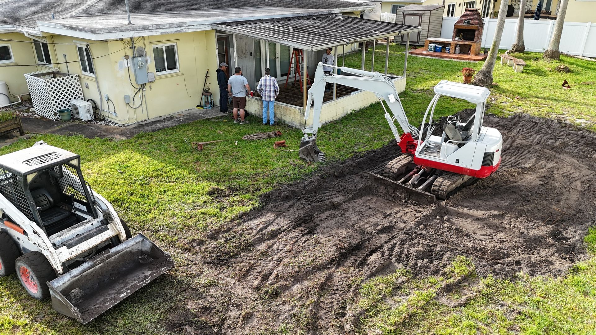 An aerial view of a bulldozer and a backhoe moving dirt in front of a house.