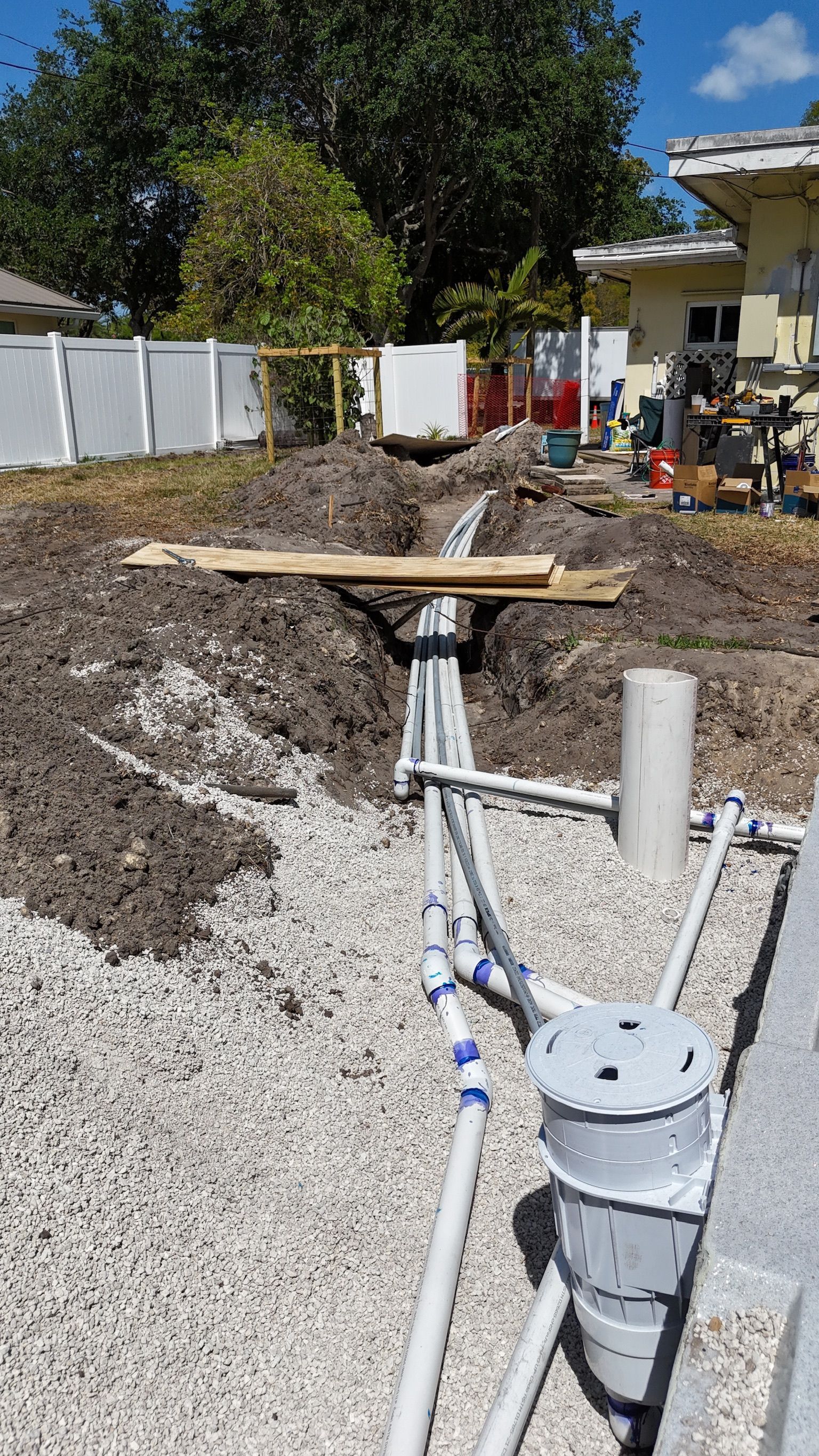 A bunch of pipes are laying in the dirt in front of a house.