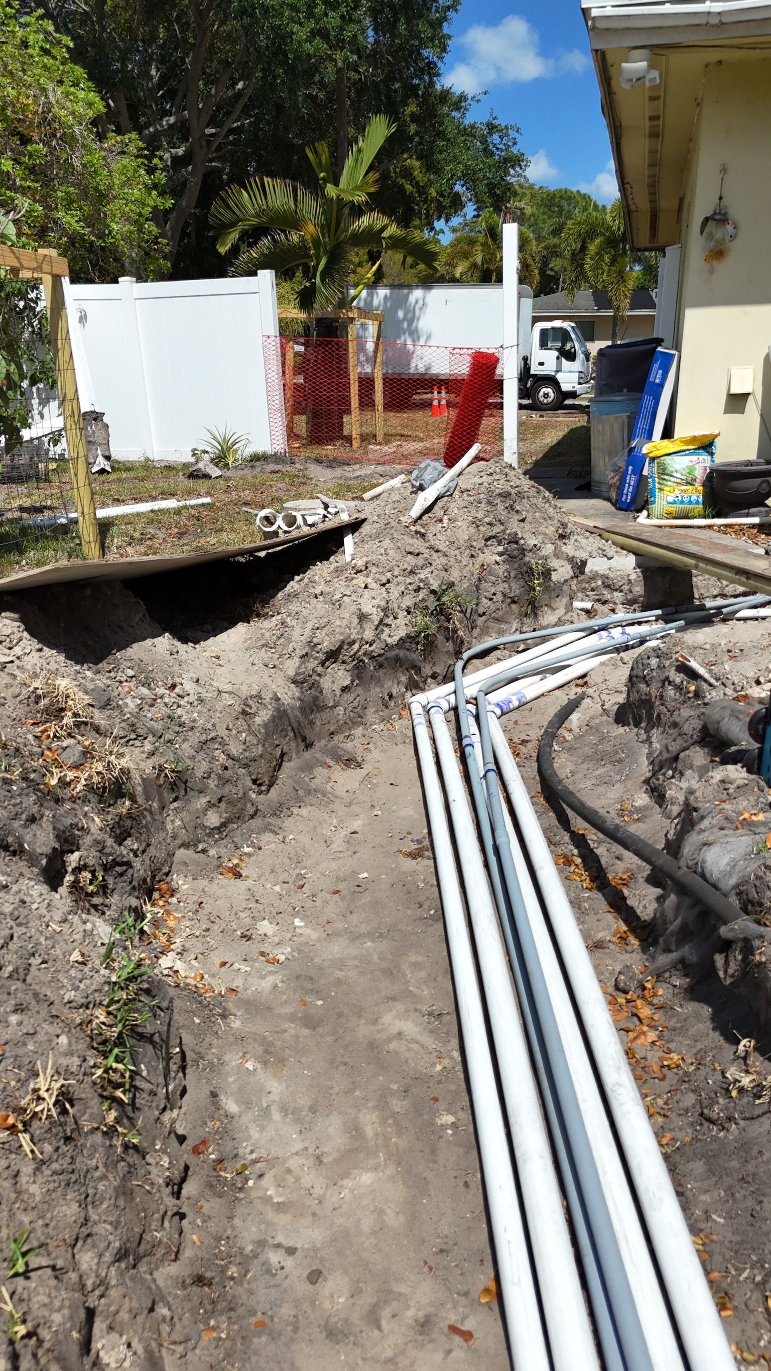 A bunch of pipes are laying in the dirt in front of a house.
