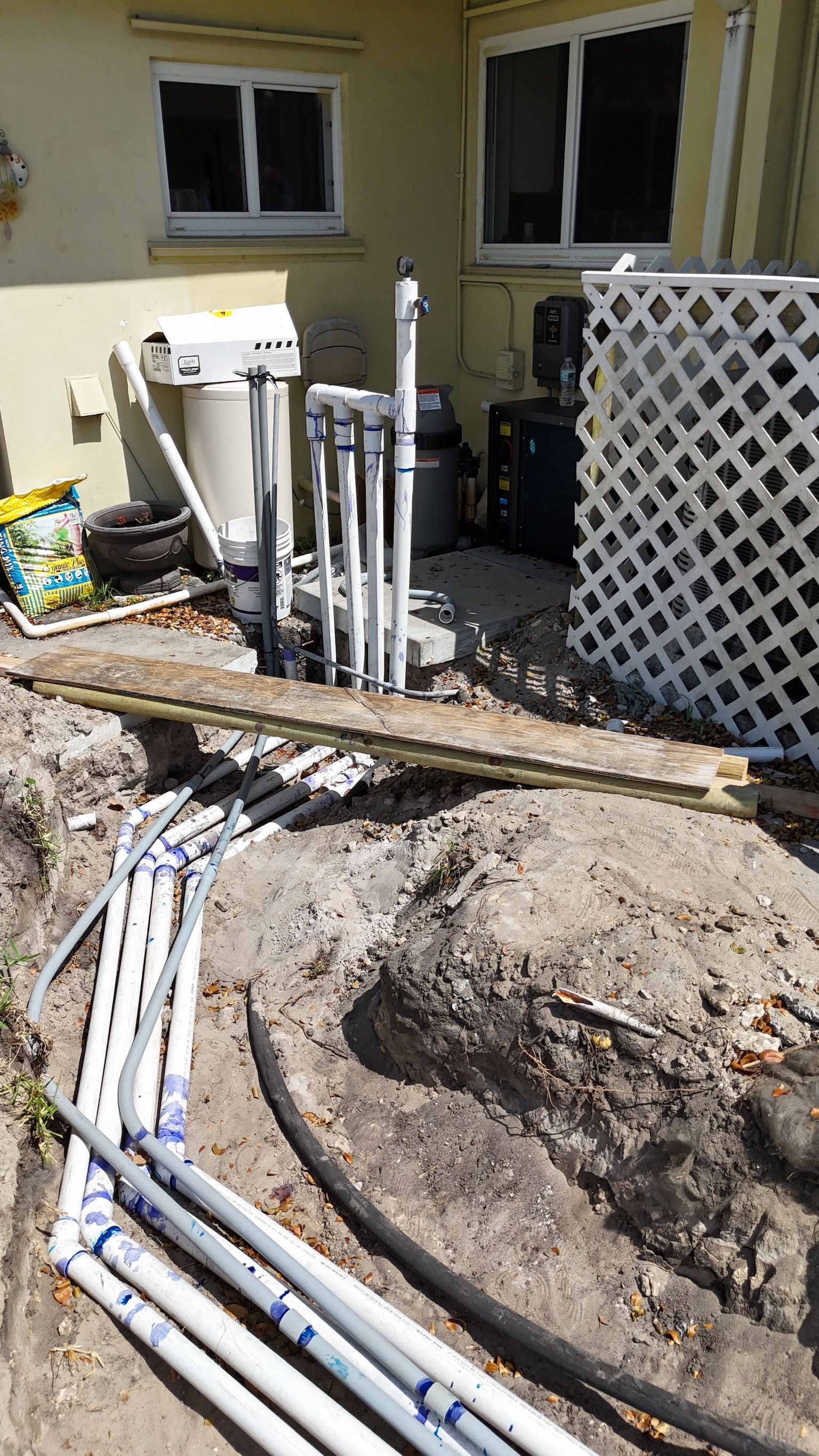 A bunch of pipes are laying in the dirt in front of a house.