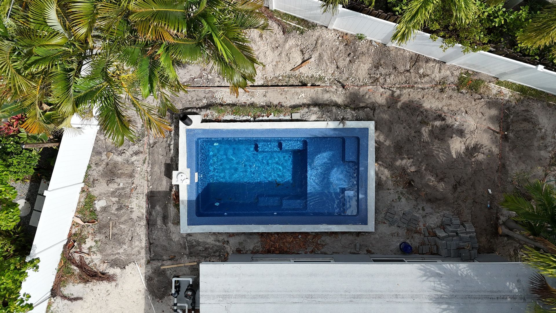 An aerial view of a swimming pool surrounded by trees and dirt.