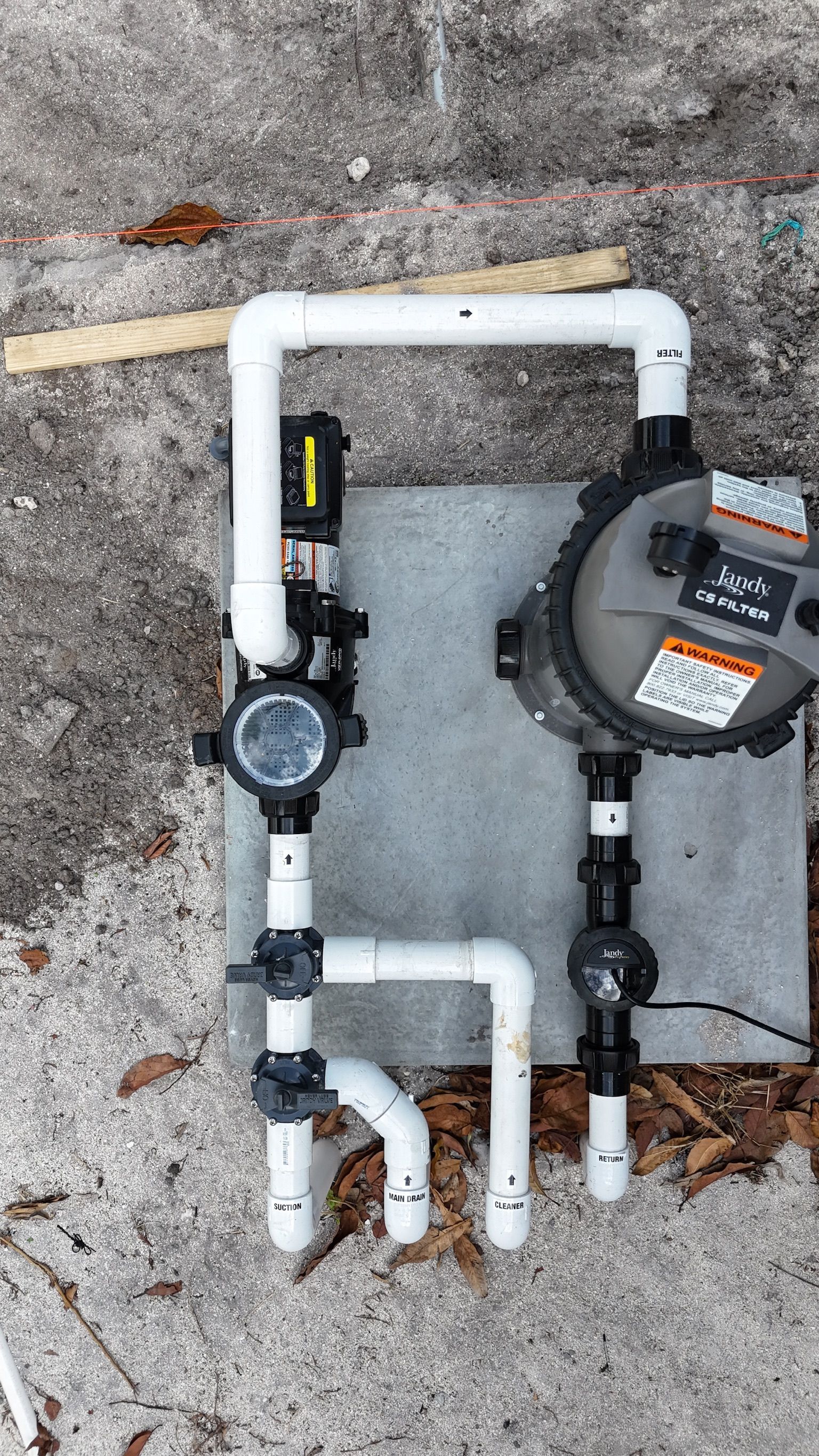 A water meter is sitting on top of a concrete surface next to some pipes.