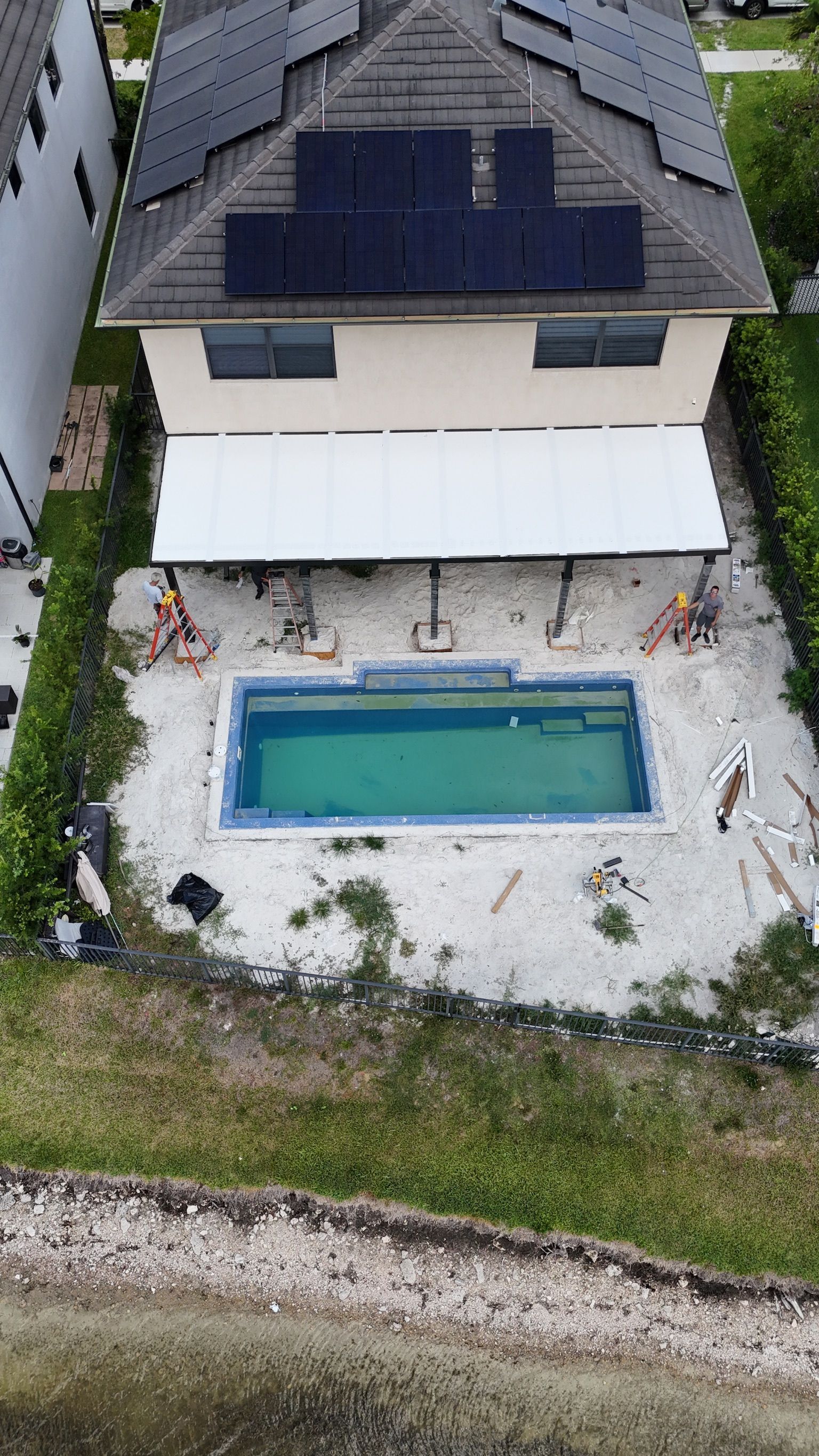 An aerial view of a house with a swimming pool and solar panels on the roof.