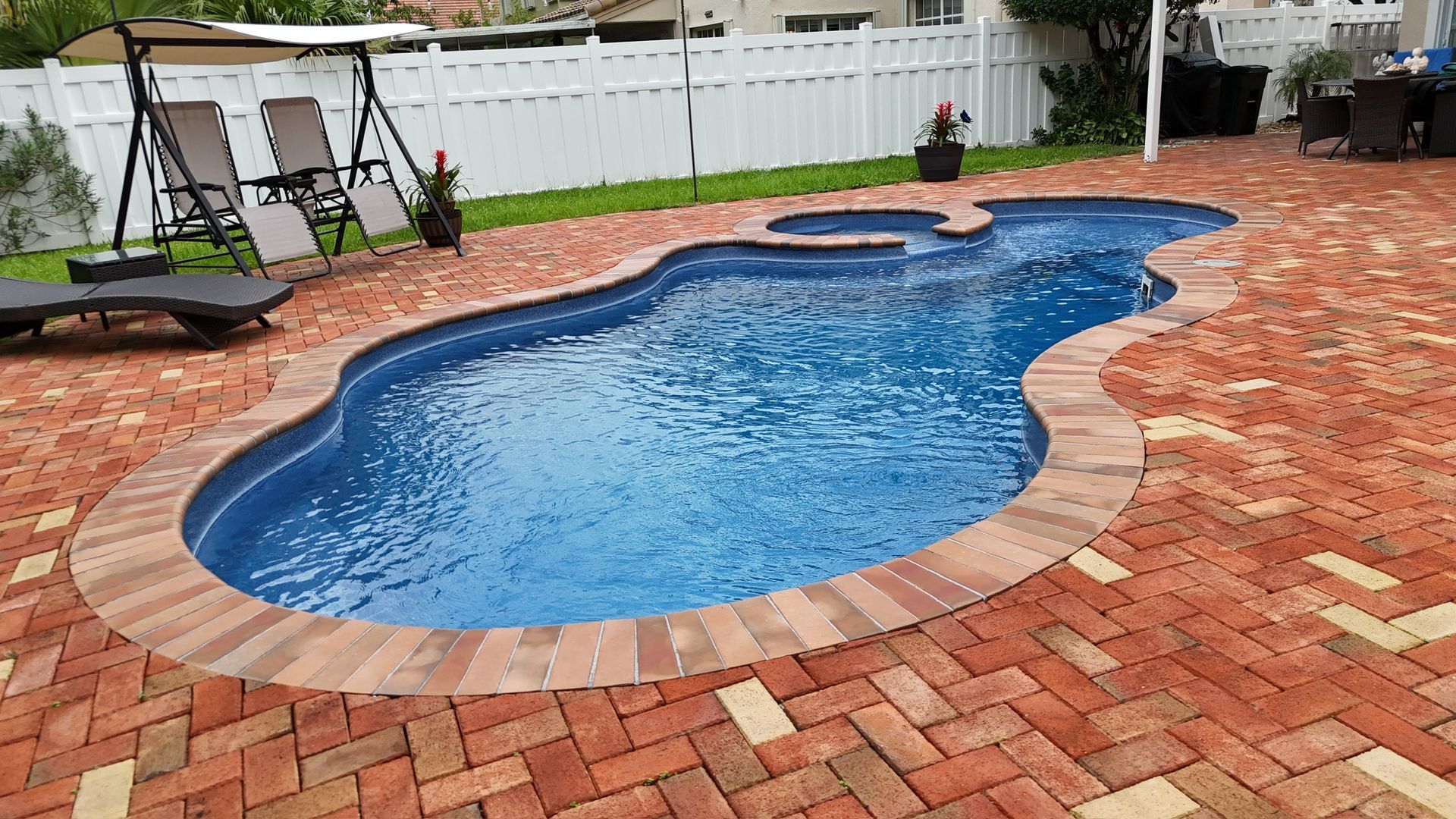 A large swimming pool is surrounded by bricks in a backyard.
