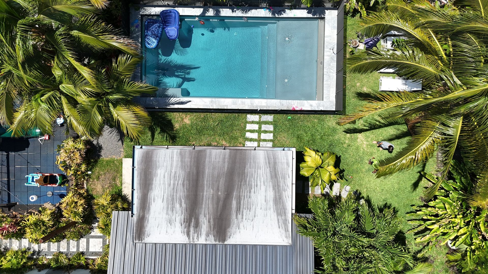 An aerial view of a house and a swimming pool surrounded by palm trees.