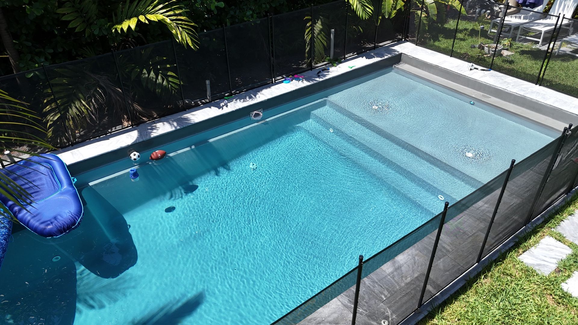 A large swimming pool surrounded by a fence and a slide.