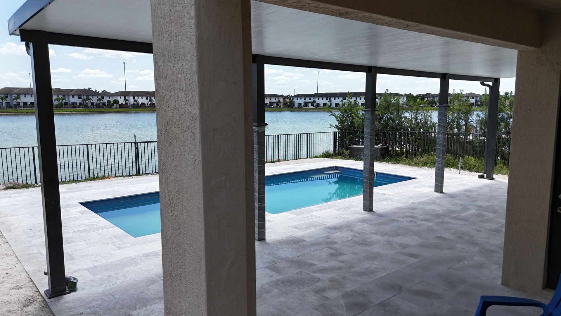 A large swimming pool is under a covered patio next to a body of water.