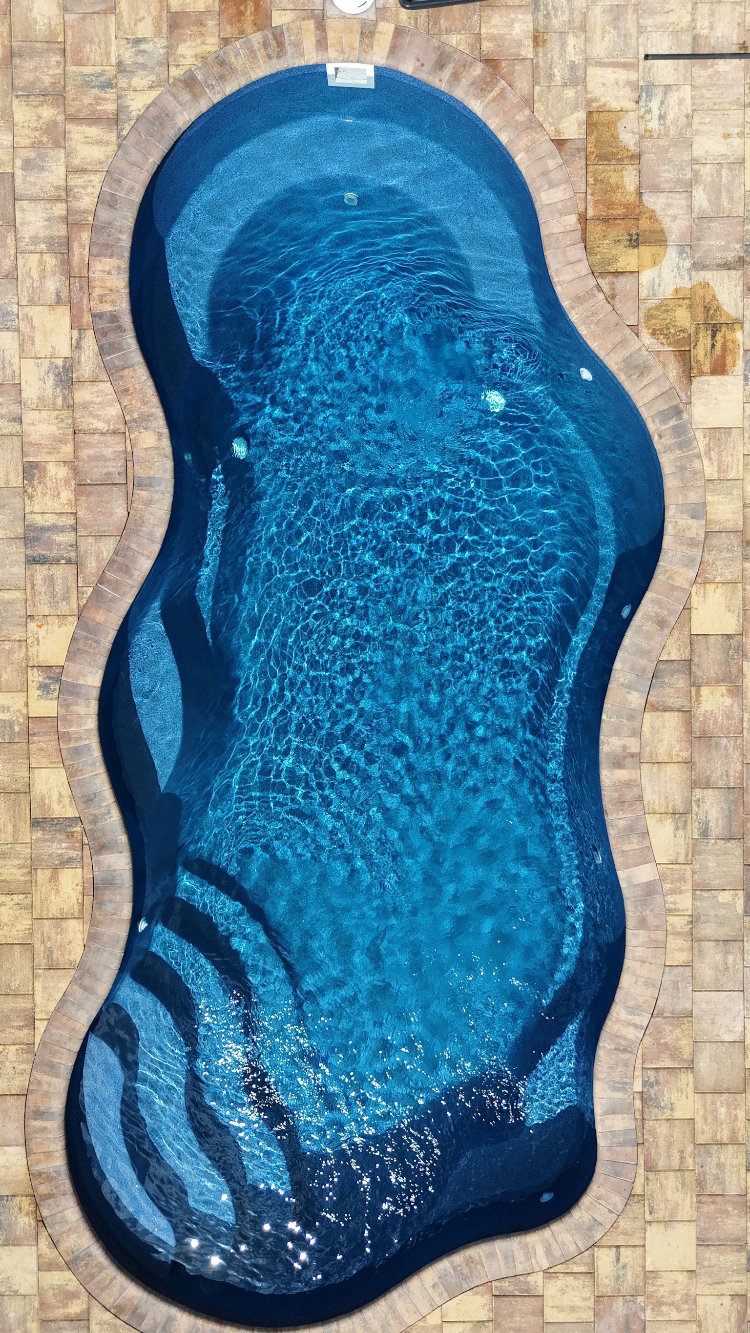 An aerial view of a large blue swimming pool on a brick patio.
