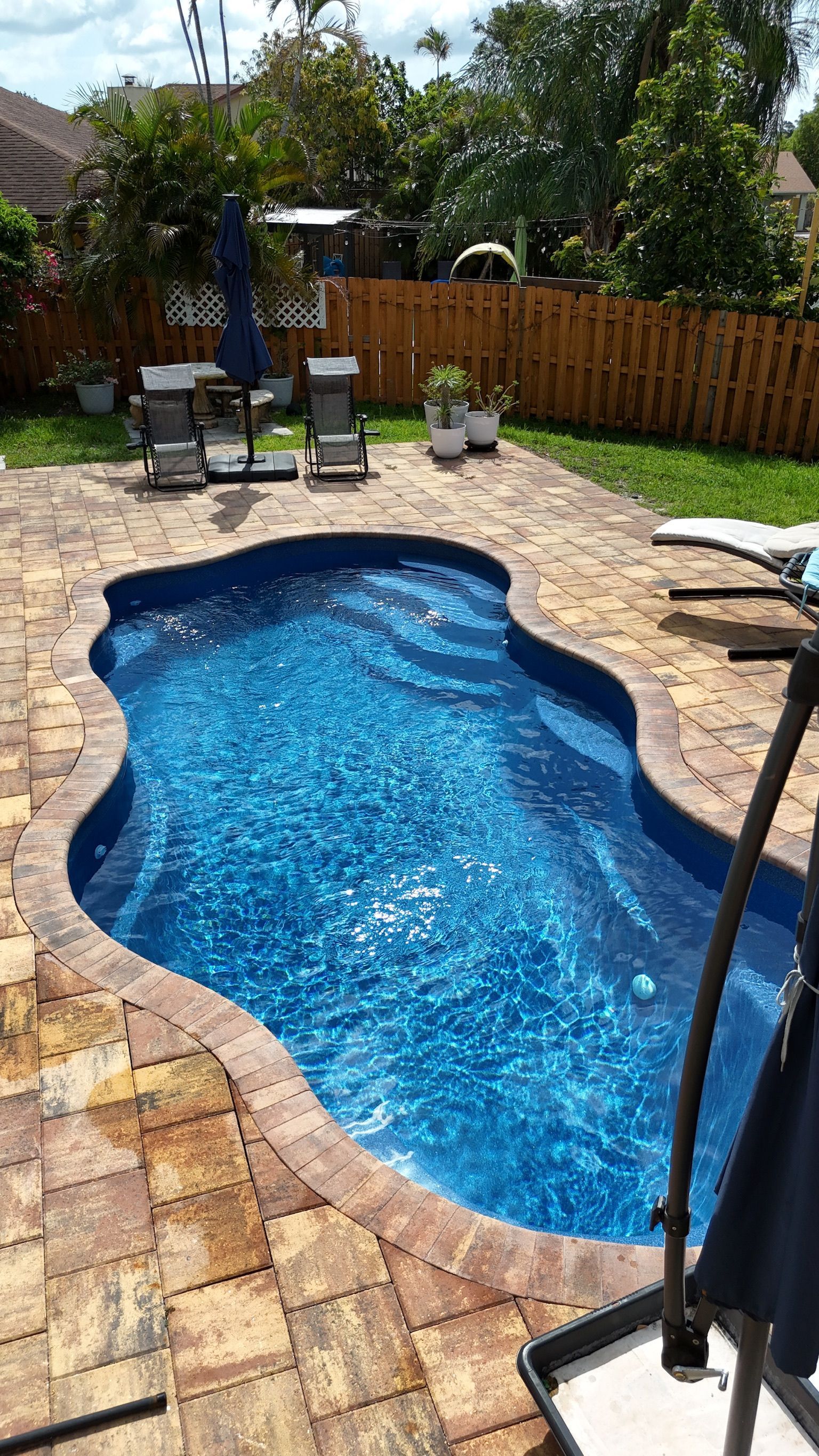 There is a large swimming pool in the backyard with chairs and umbrellas.
