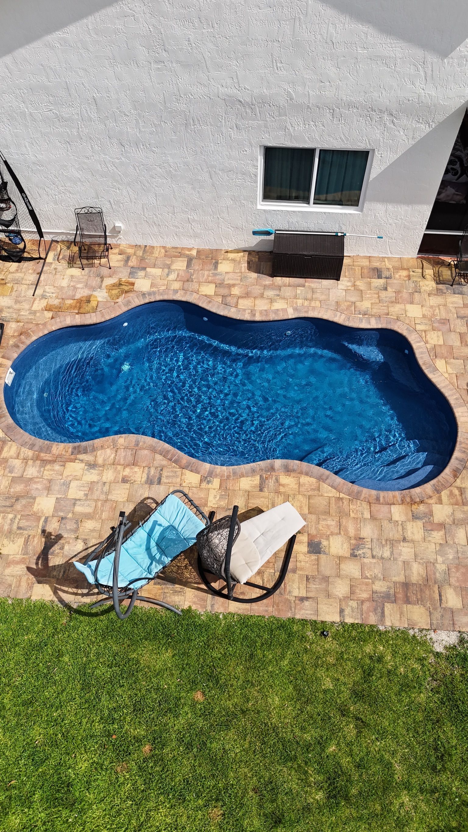 A large swimming pool is sitting on top of a brick patio next to a house.