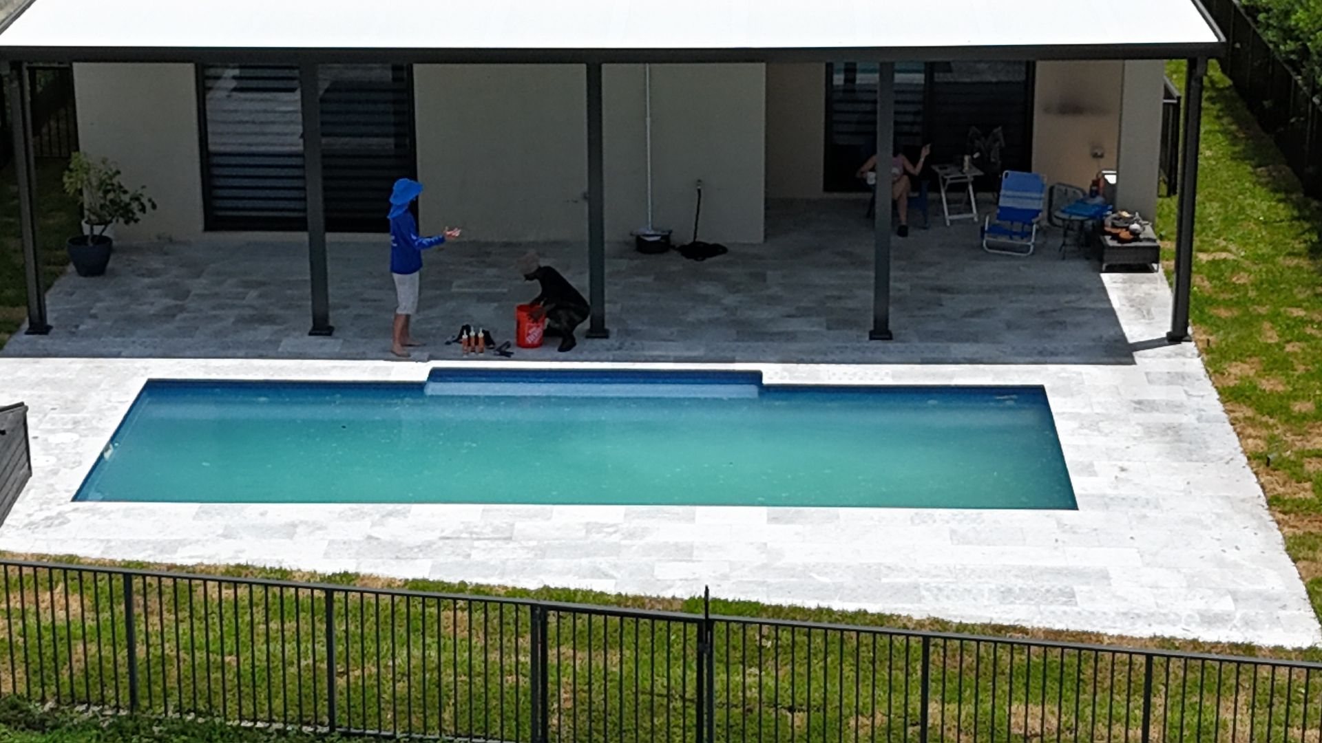 A man is standing next to a swimming pool in front of a house.