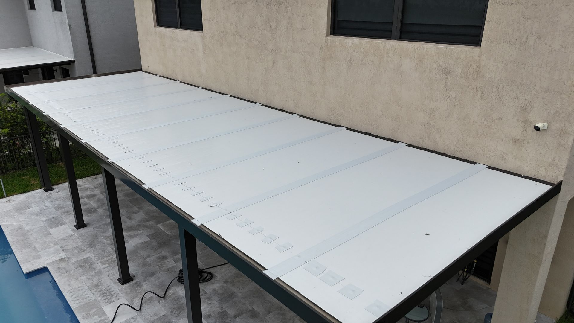 A white canopy is sitting on the side of a house next to a pool.