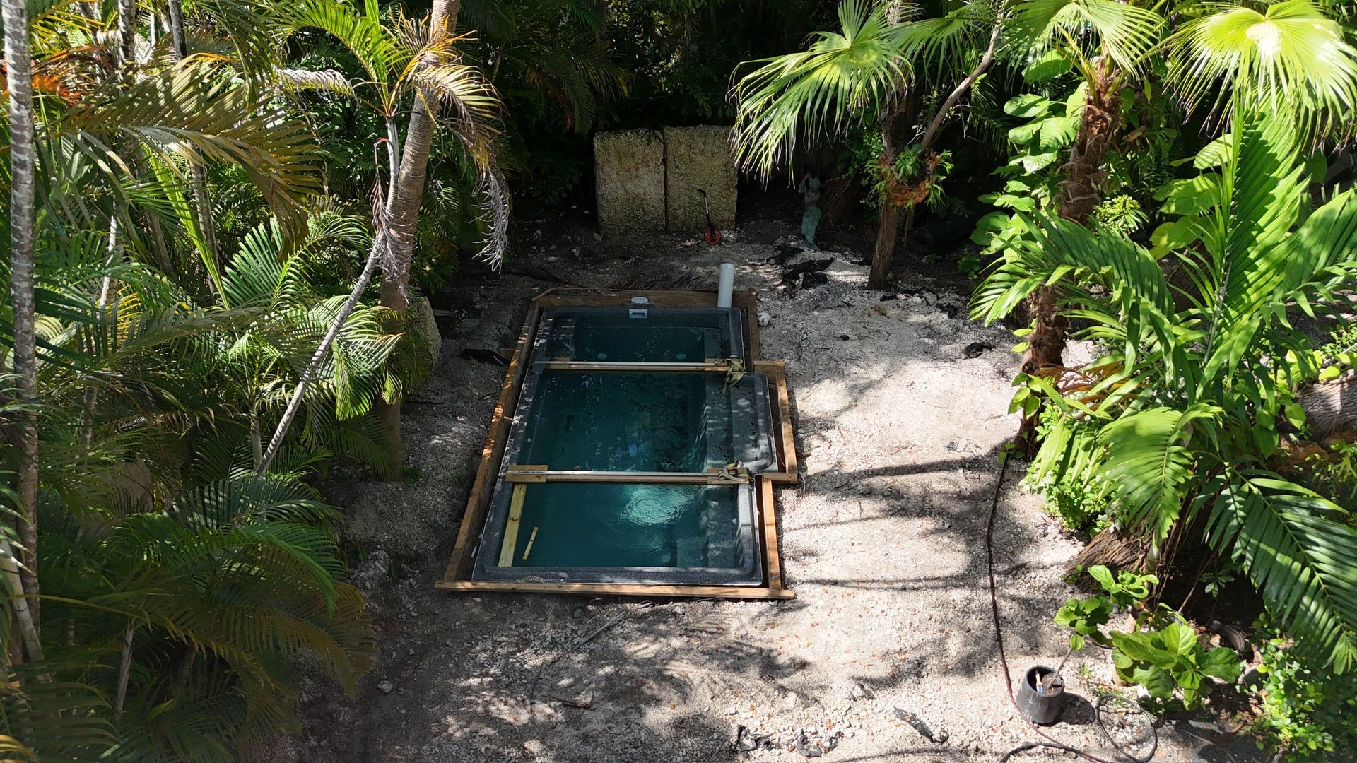 An aerial view of a swimming pool in the middle of a lush green forest.