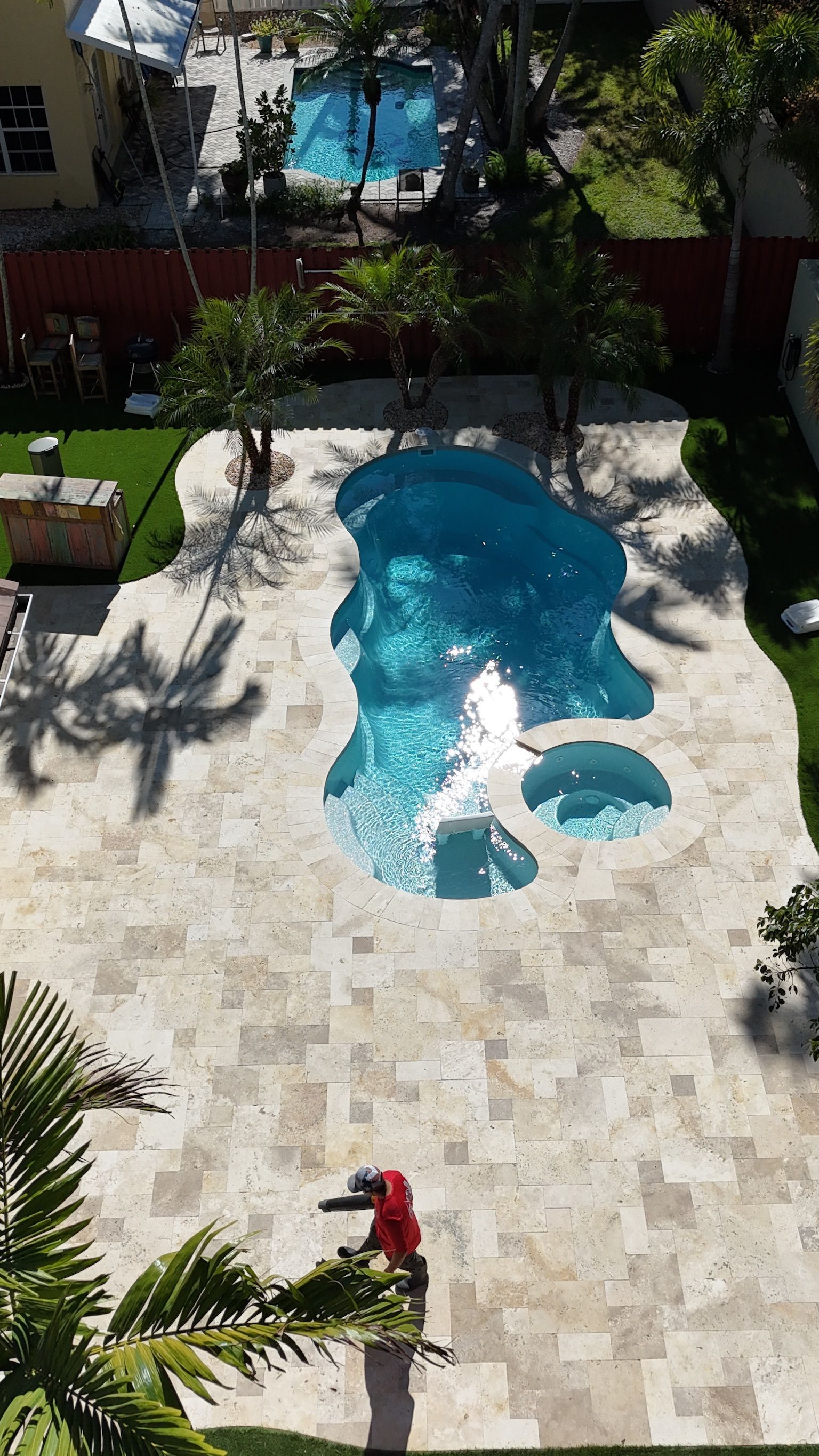 An aerial view of a large swimming pool in a backyard surrounded by palm trees.