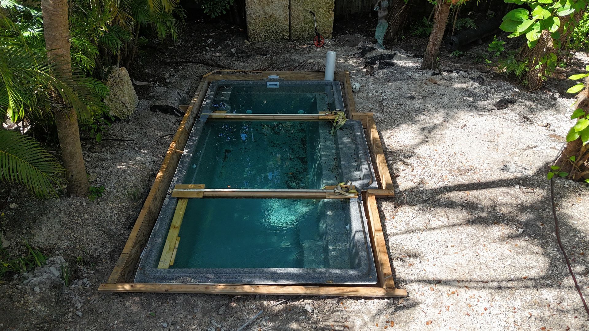 A small swimming pool is surrounded by trees and gravel.
