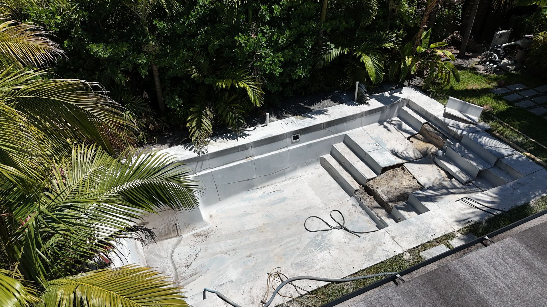 An aerial view of an empty swimming pool surrounded by palm trees.