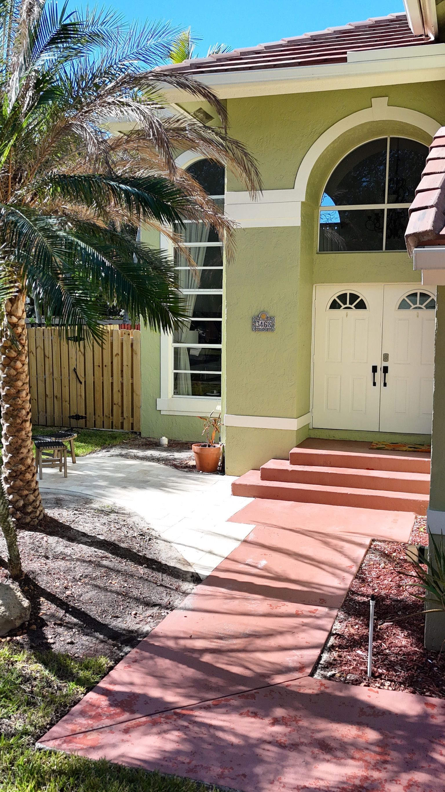 A house with a palm tree in front of it and a walkway leading to it.