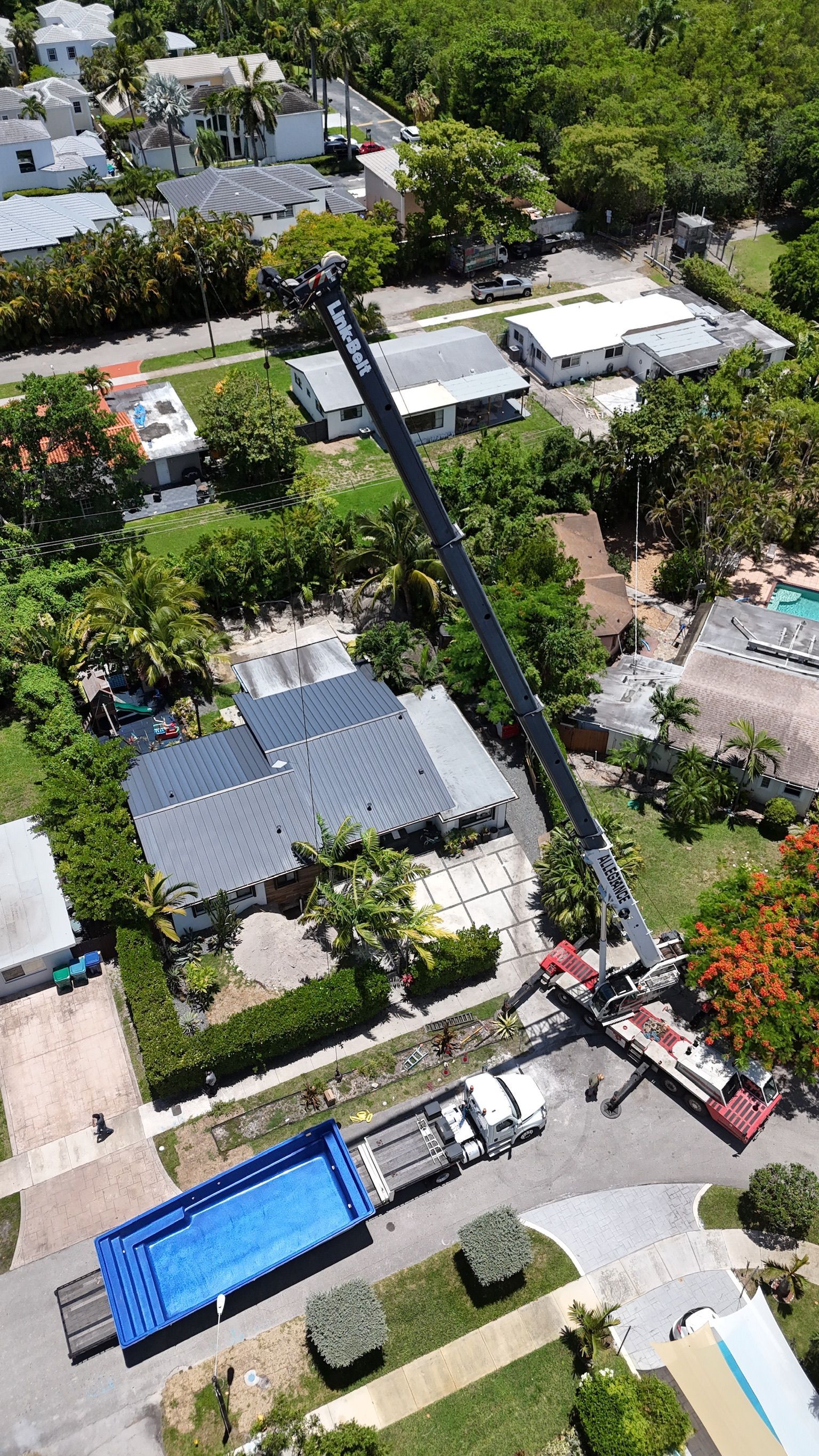 An aerial view of a crane lifting a large blue container in a residential area.