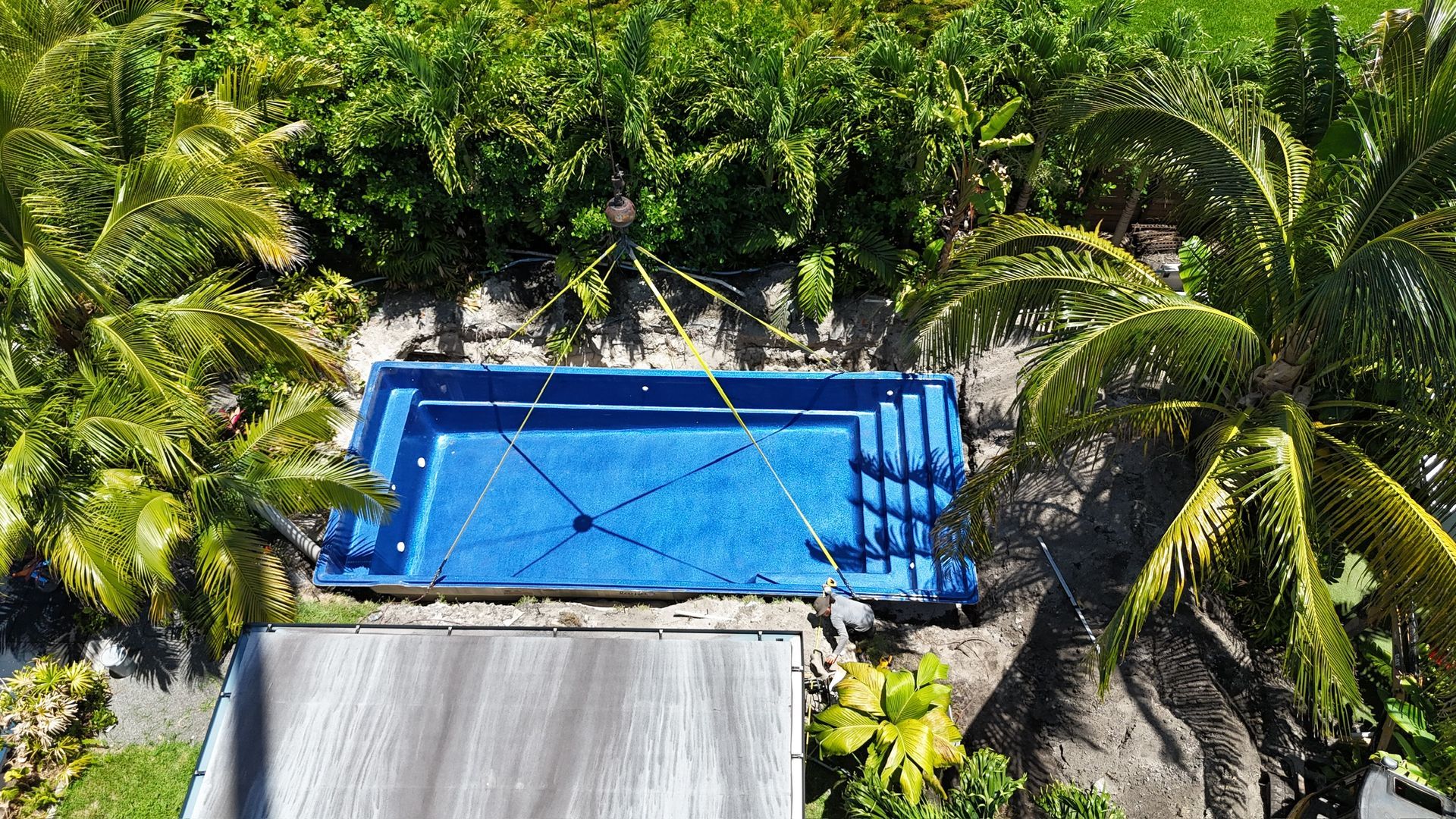 An aerial view of a large blue swimming pool surrounded by palm trees.