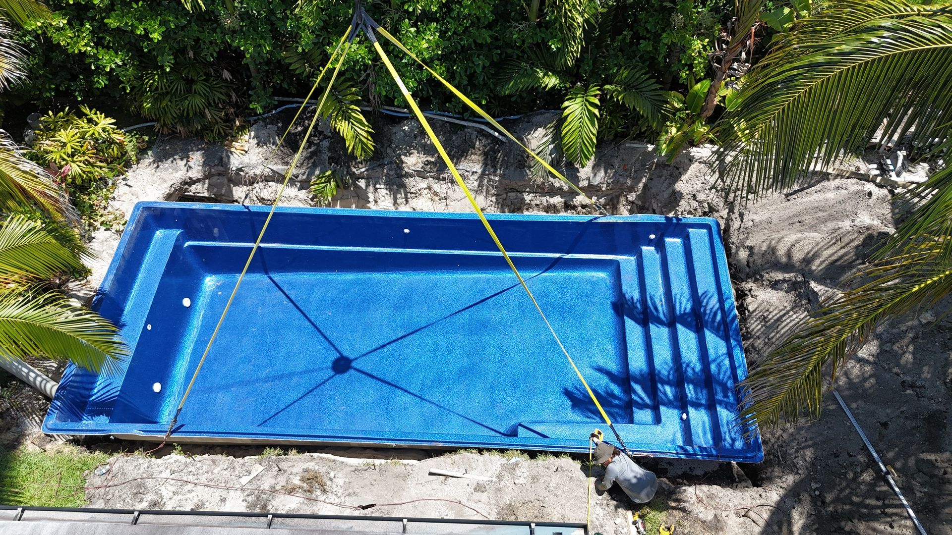 An aerial view of a blue swimming pool being lifted by a crane.