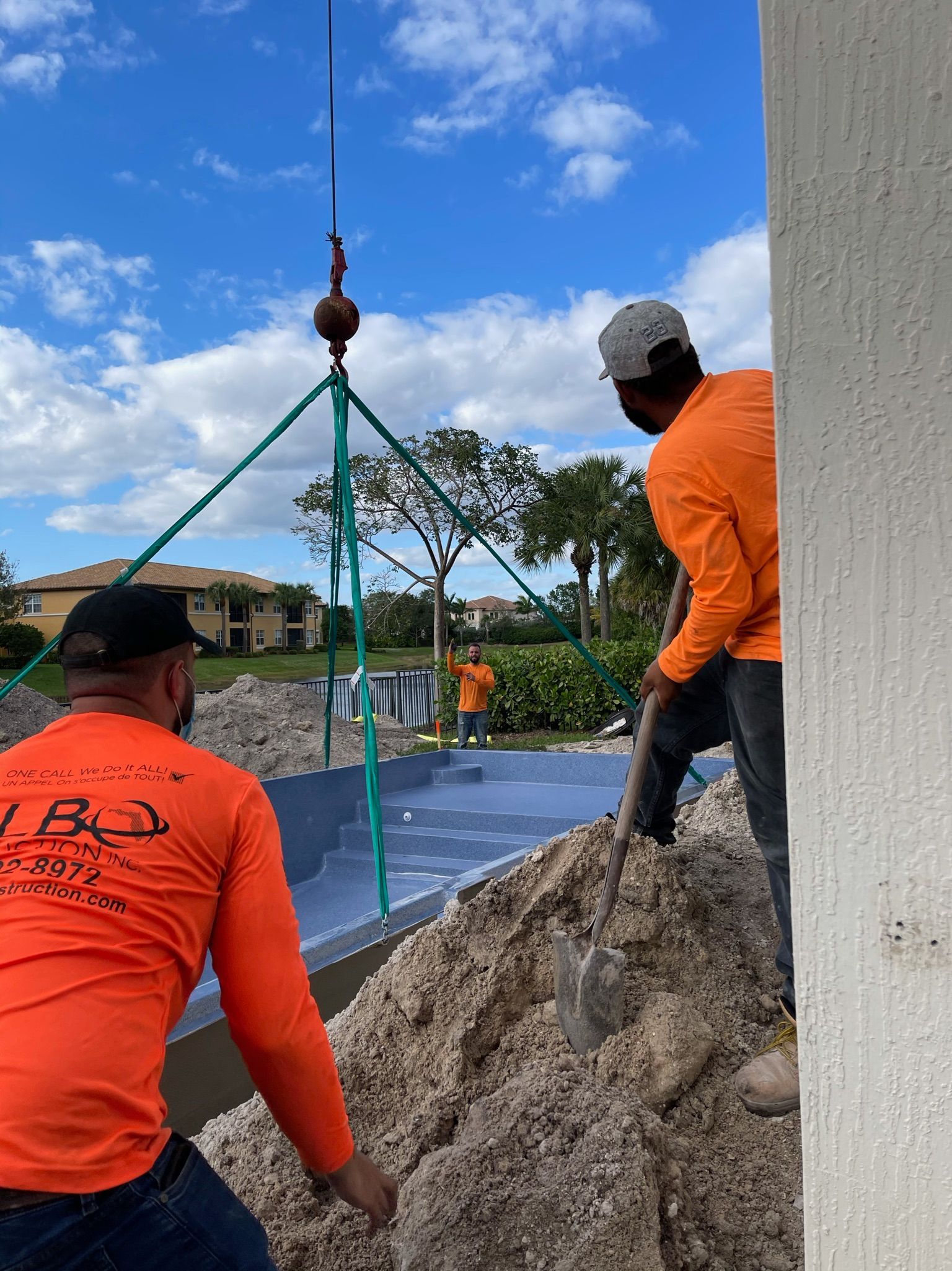 A man in an orange shirt is standing next to a pile of dirt.