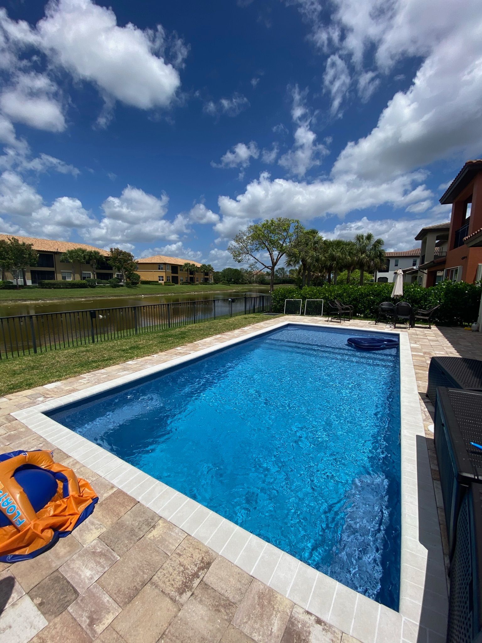 A large swimming pool is surrounded by buildings and a lake.
