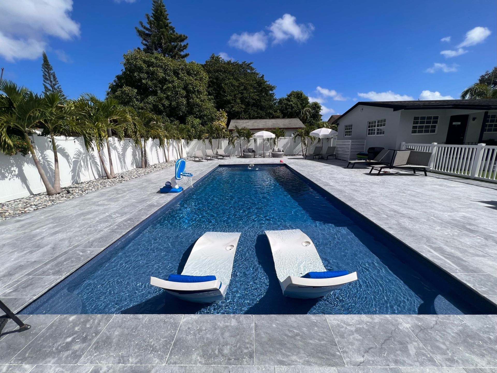 A large swimming pool with two chairs in it and a house in the background.