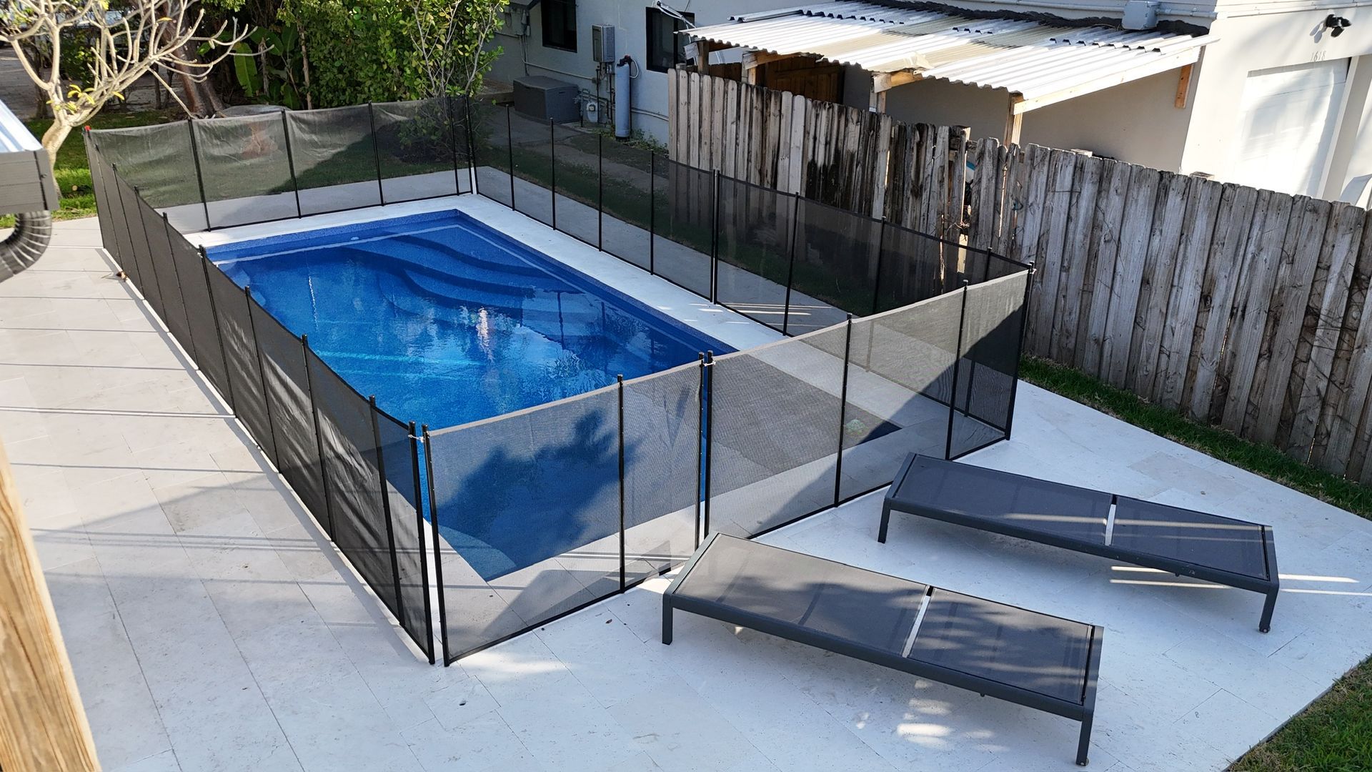 A fence surrounds a large swimming pool in a backyard.