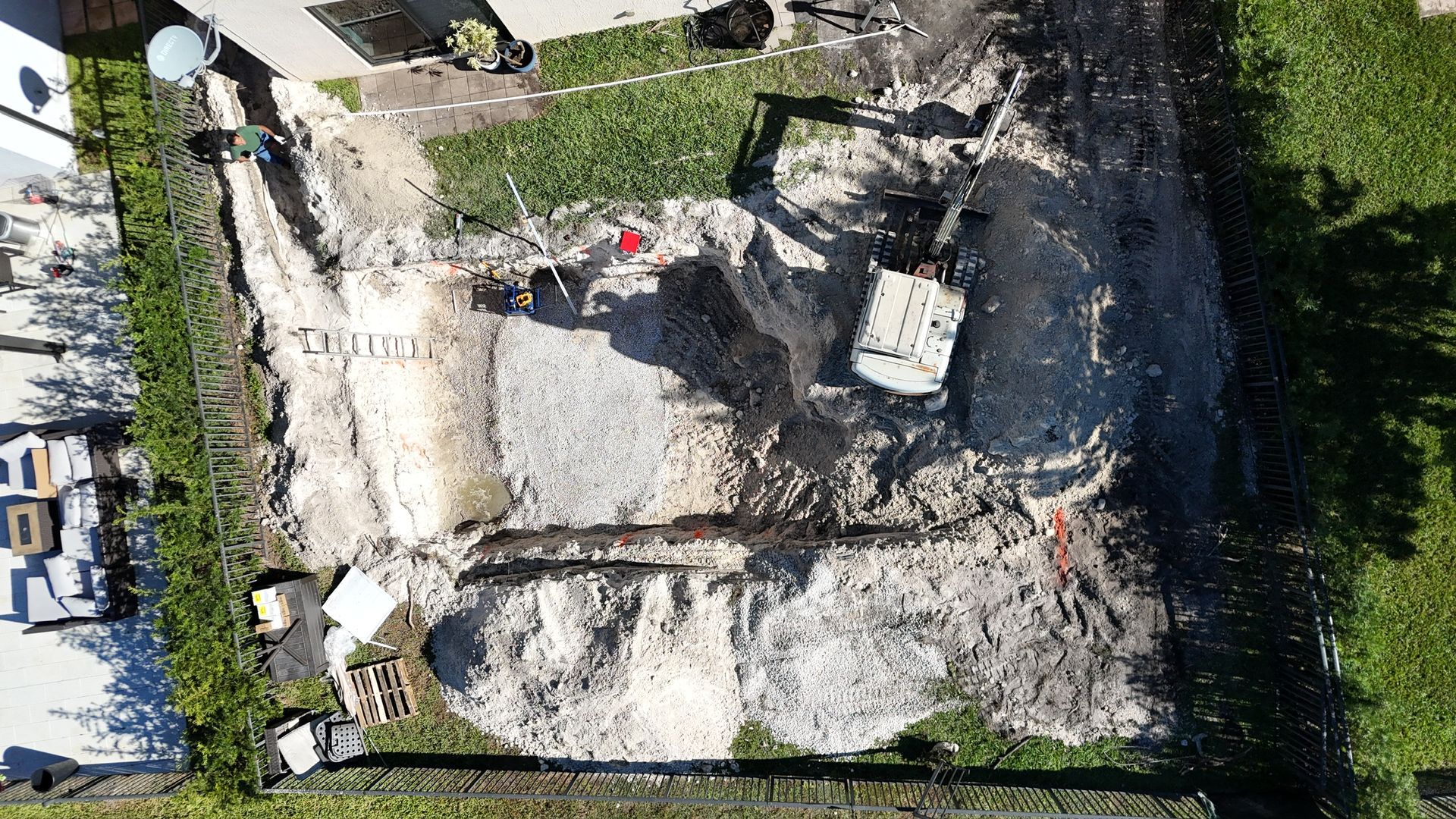 An aerial view of a house with a white excavator digging the ground