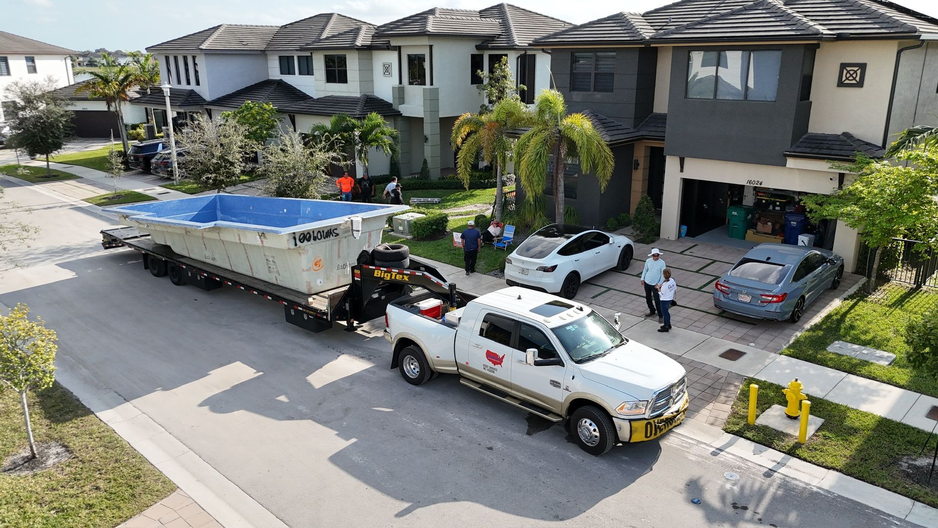 An aerial view of a truck pulling a swimming pool down a street.