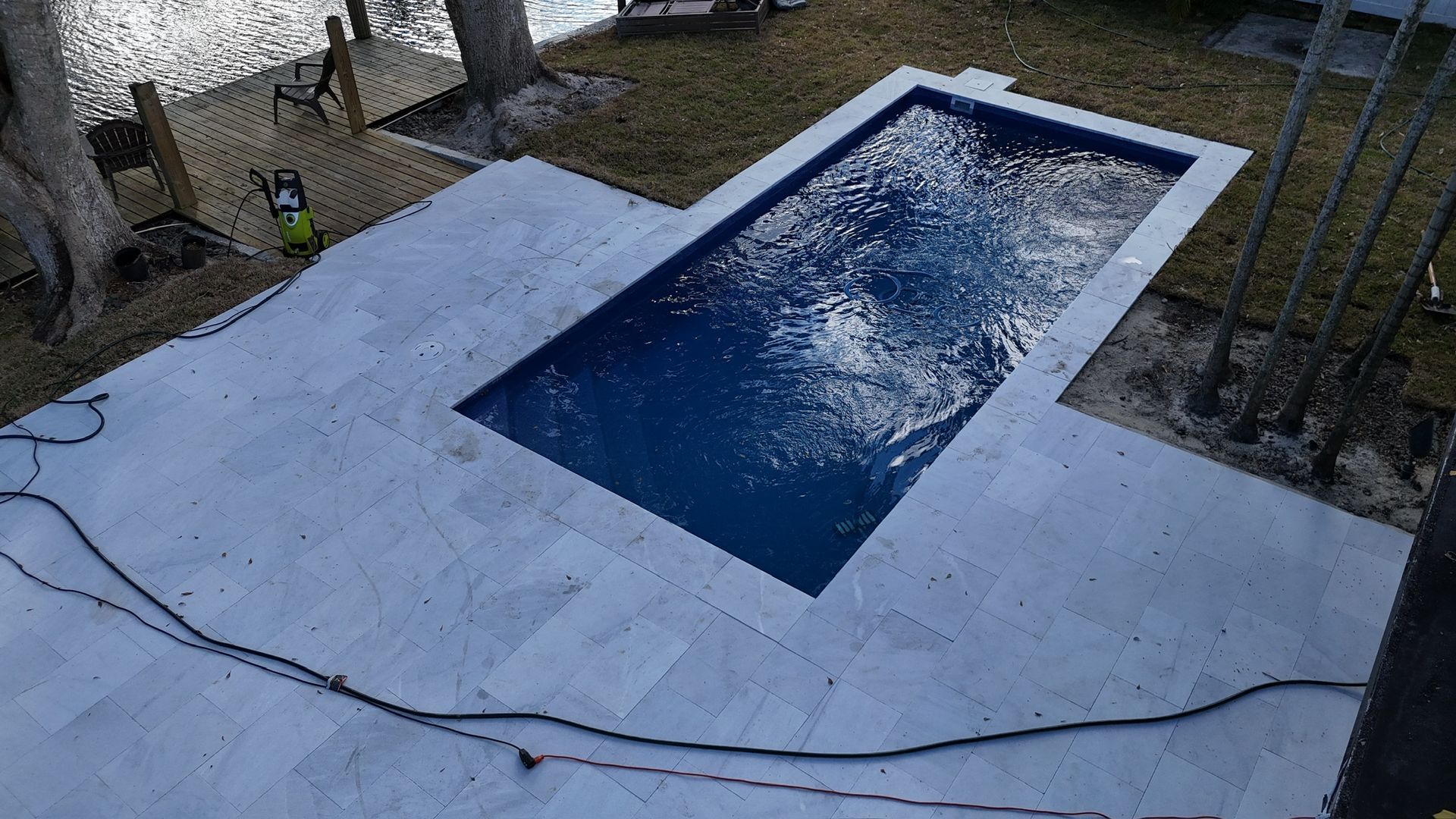 A large swimming pool is sitting on top of a tiled patio next to a body of water.