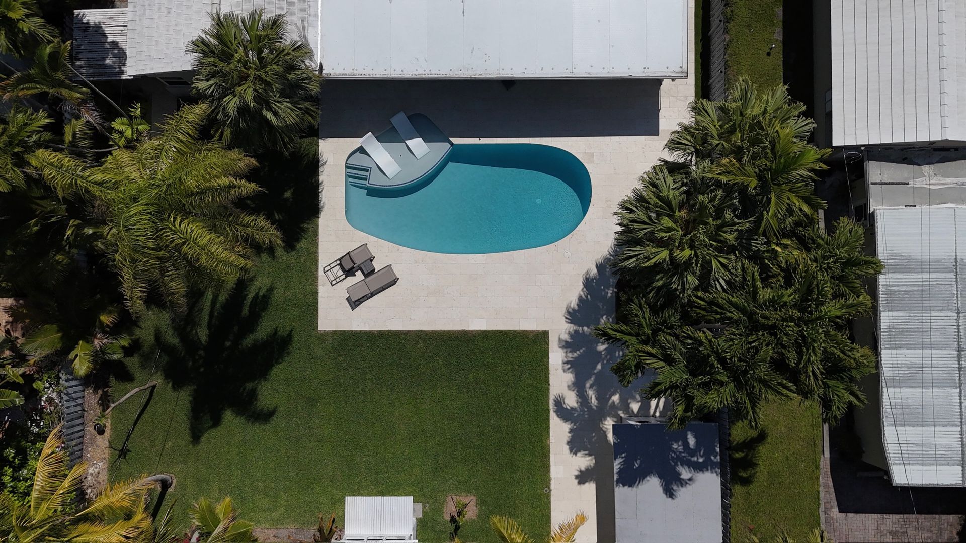 An aerial view of a house with a swimming pool in the backyard surrounded by palm trees.