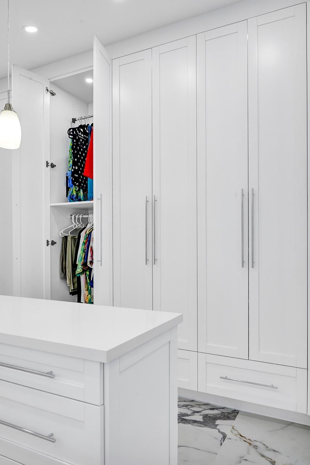 A walk in closet with white cabinets and drawers and a large island in the middle.