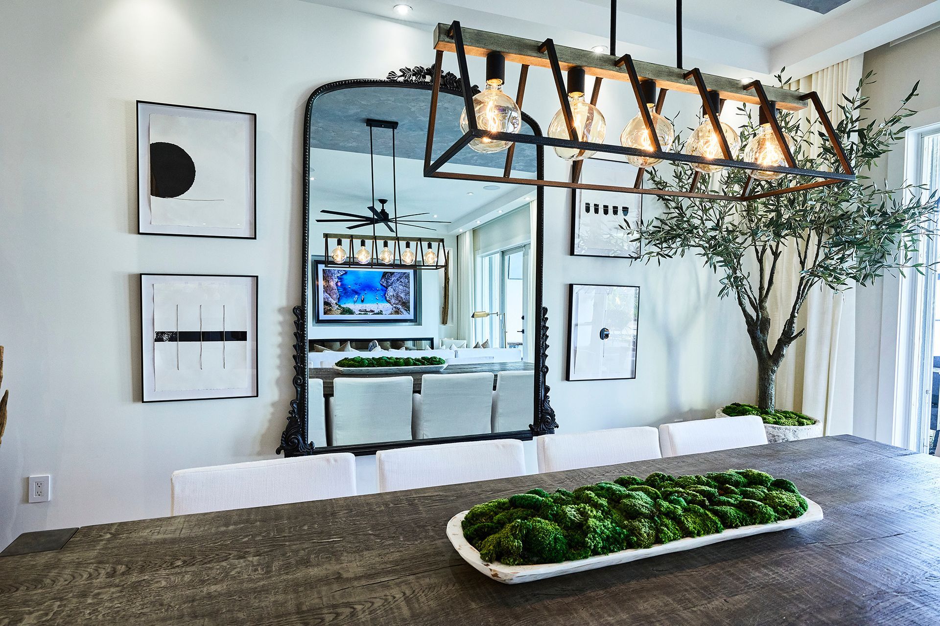 A dining room with a large mirror and a tray of moss on the table.