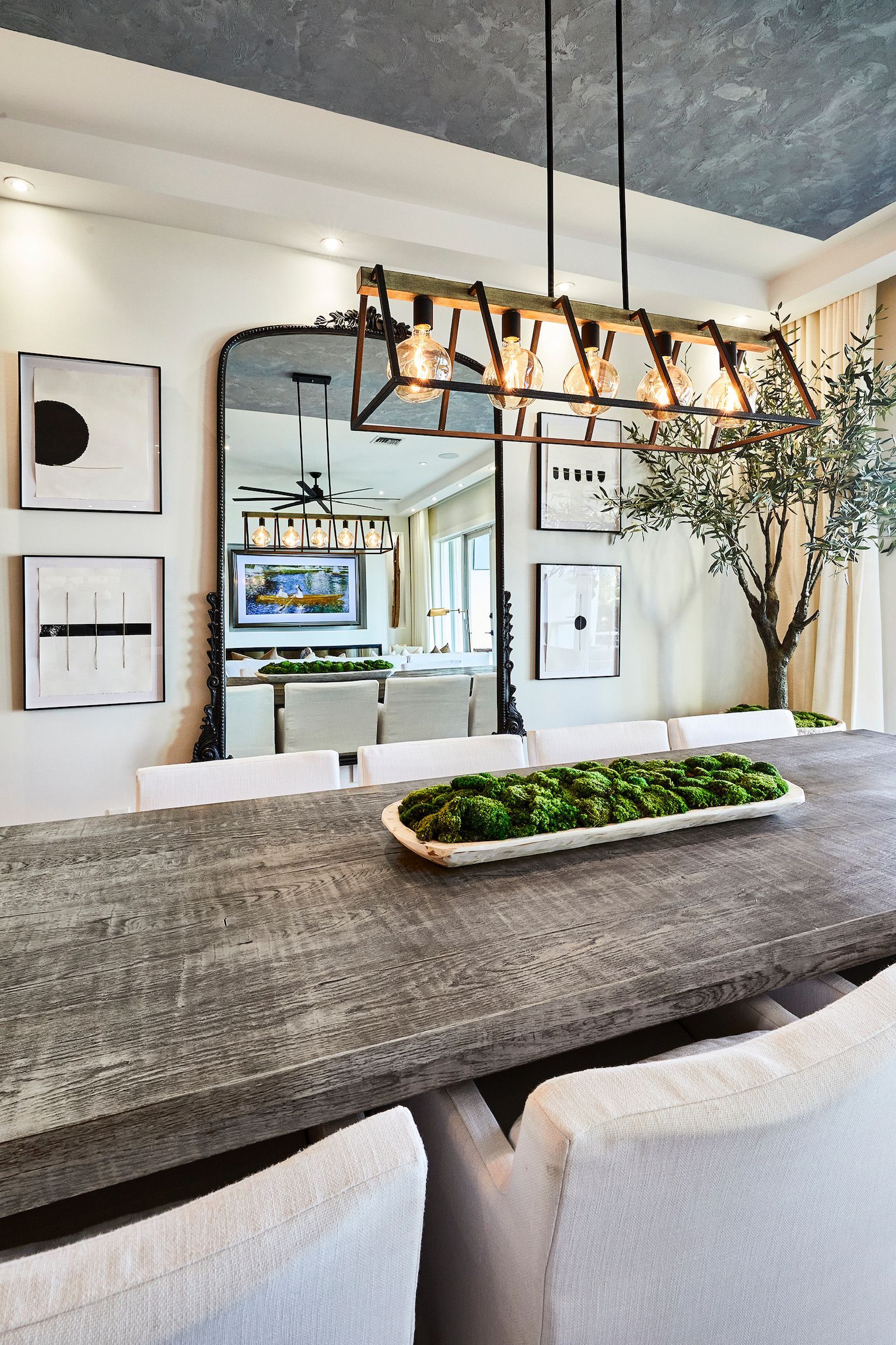 A dining room with a long table and chairs and a large mirror.