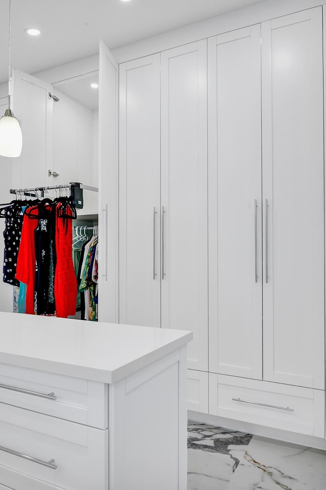 A walk in closet with white cabinets , drawers , and a large island.