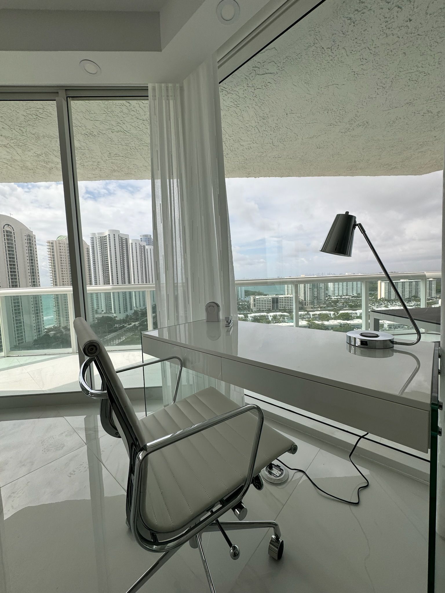 A white chair is sitting in front of a desk in a room with a large window.
