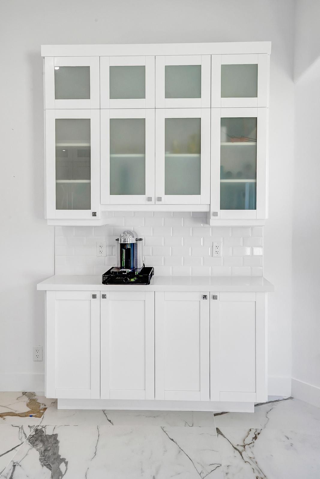 A kitchen with white cabinets and a marble floor.