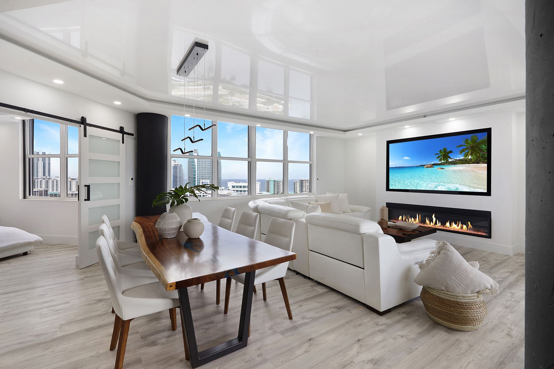 A living room with a dining table and chairs and a flat screen tv on the wall.