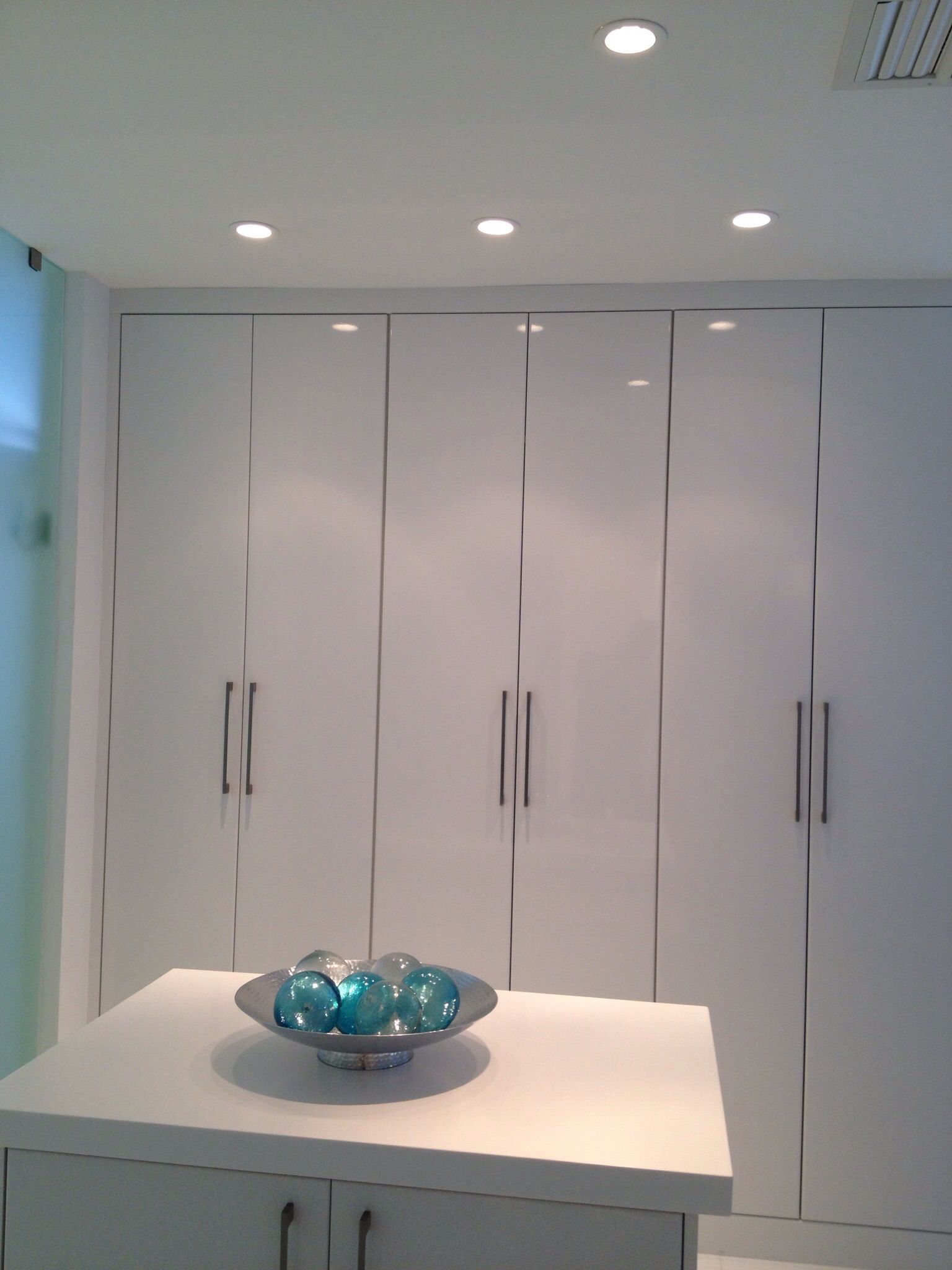 A bowl of blue balls sits on a table in front of a wall of white cabinets