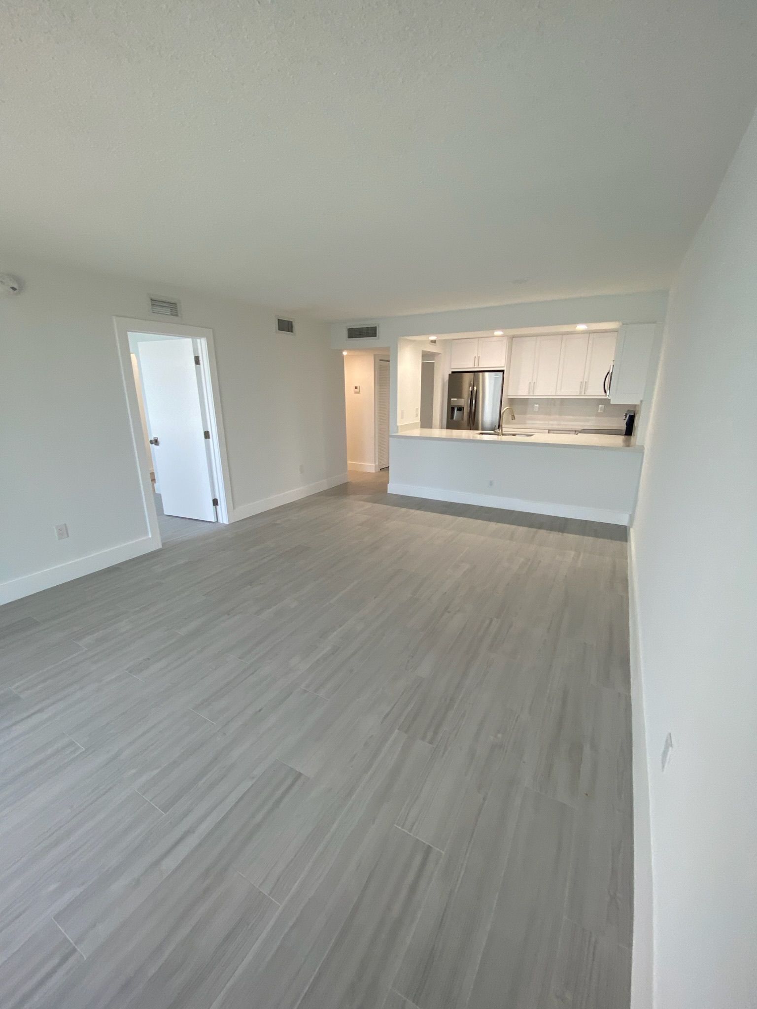 An empty living room with a kitchen in the background.