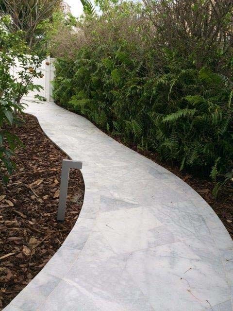 A curved concrete walkway leading to a white gate surrounded by trees and bushes.