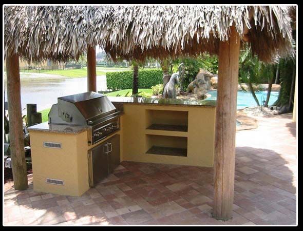 An outdoor kitchen with a thatched roof and a grill